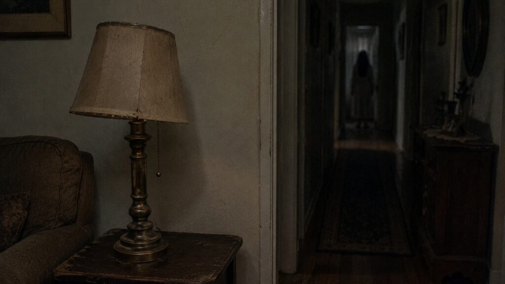 Fictional evidence image of an old table lamp illuminating a dark hallway where a figure appears in the distance.